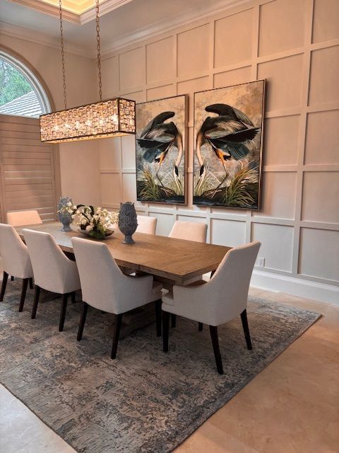Elegant dining room with a wooden table, eight white chairs, two bird paintings, and a rectangular chandelier.