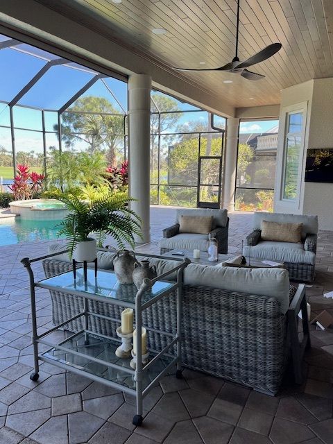 Outdoor patio with pool. Gray wicker furniture, bar cart, and screened enclosure overlooking greenery.
