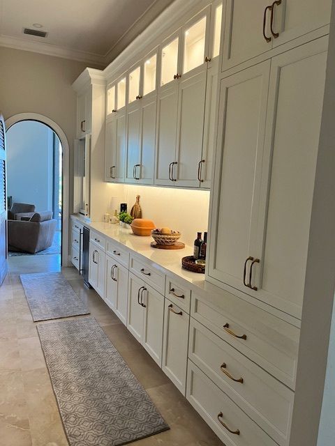 White pantry with long countertop, cabinets, arched doorway, and runner rugs.