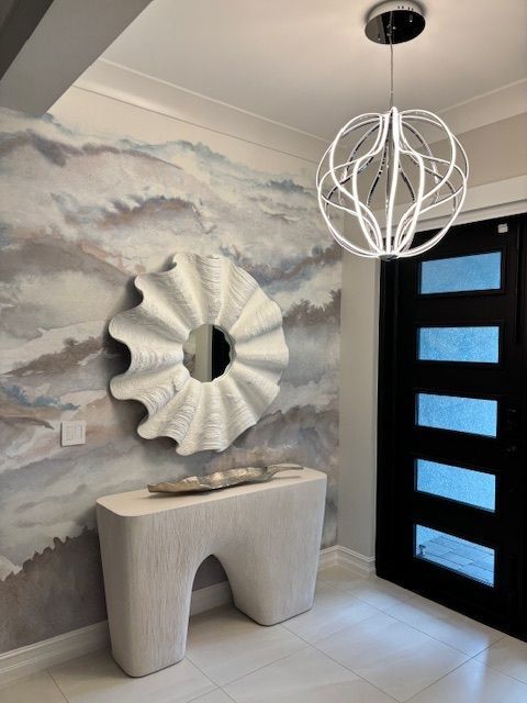 Entryway with a white console table, seashell mirror, and abstract wallpaper. Black door and modern pendant light.