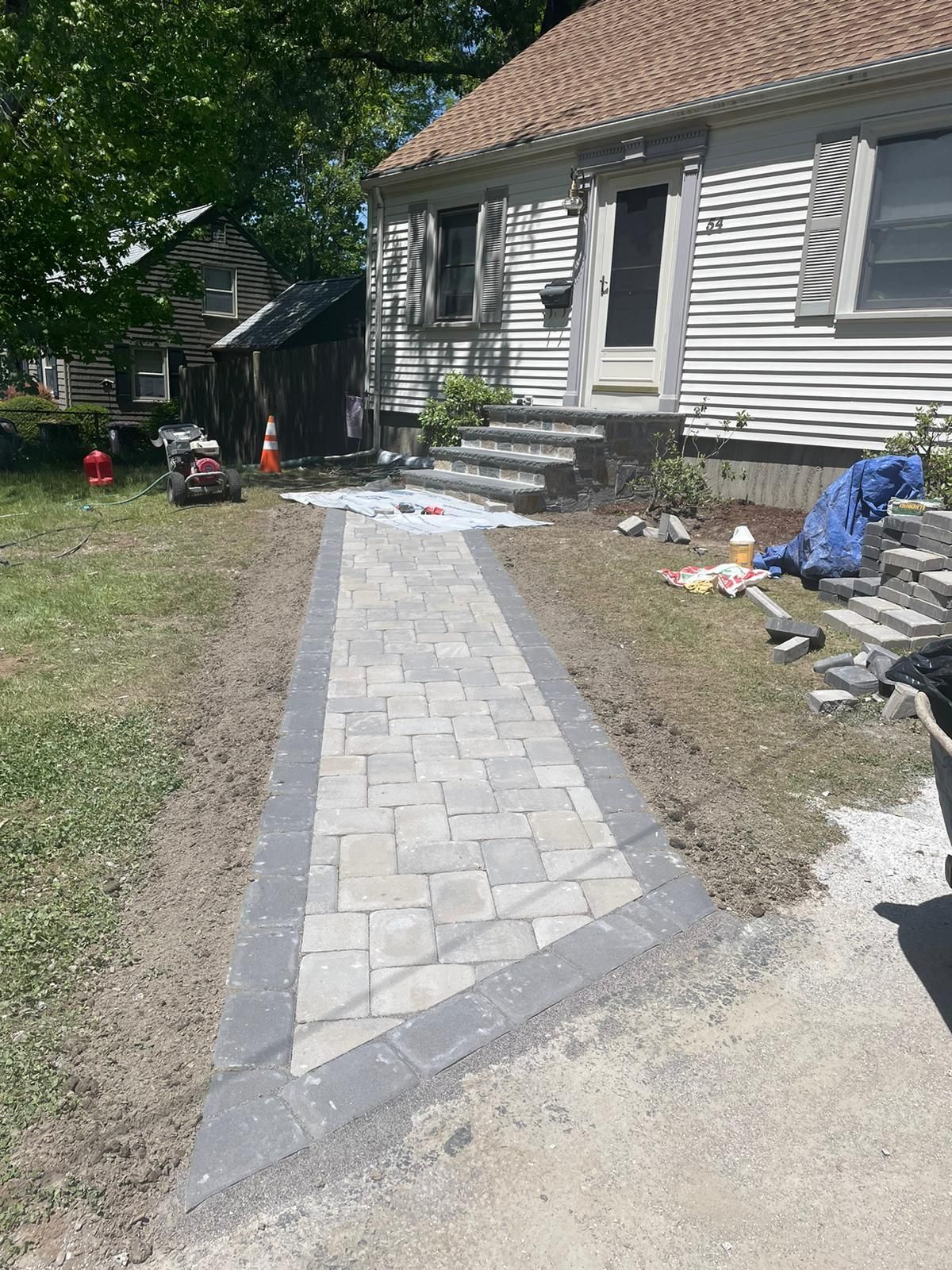 A new paved walkway made of light-colored rectangular stones with a dark border leading to a residential house front door.