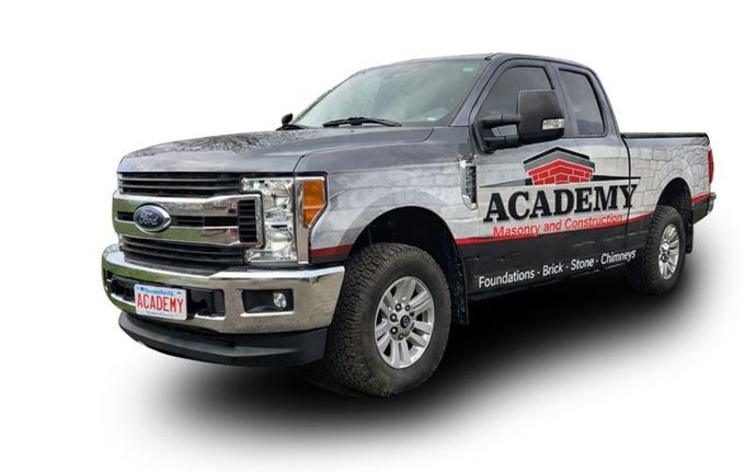 A grey Ford pickup truck branded with 'Academy Masonry and Construction' logos and text on its side.
