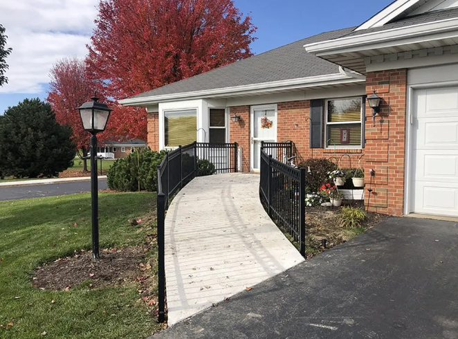Ramp leading to a brick building's entrance, black railings, lamp post, red autumn tree, driveway.