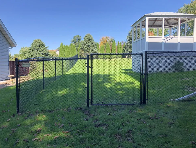 Black chain-link fence with gate, enclosing grassy backyard with gazebo under a clear, sunny sky.