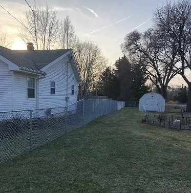 A white house with a chain-link fence in a yard at sunset. Shed visible.