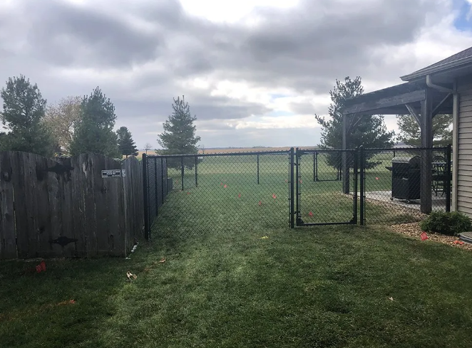 Backyard with chain-link fence and open gate, leading to open space. Cloudy sky.