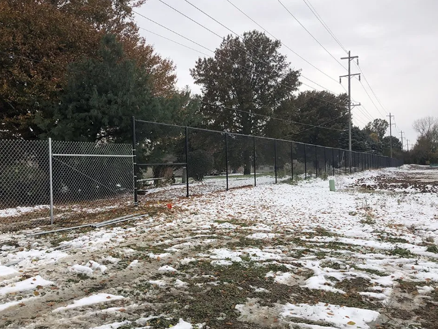 Chain-link fence in a snow-covered field, with trees and power lines in the background.
