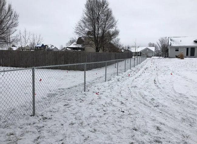 A chain-link fence lines a snow-covered yard on a cloudy day.