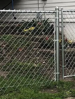 Chain-link fence in front of a garden bed with plants and a section open for access.