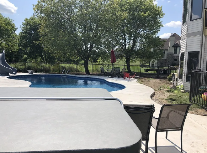 Poolside scene with a pool, water slide, patio, and partially visible house and trees.