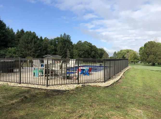 A fenced-in above-ground pool surrounded by grass and trees under a cloudy sky.