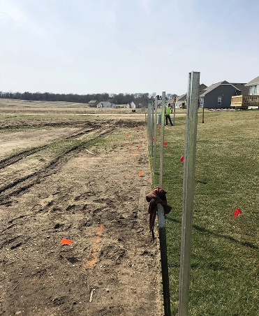 Fence posts being installed in an open field; worker in the distance.