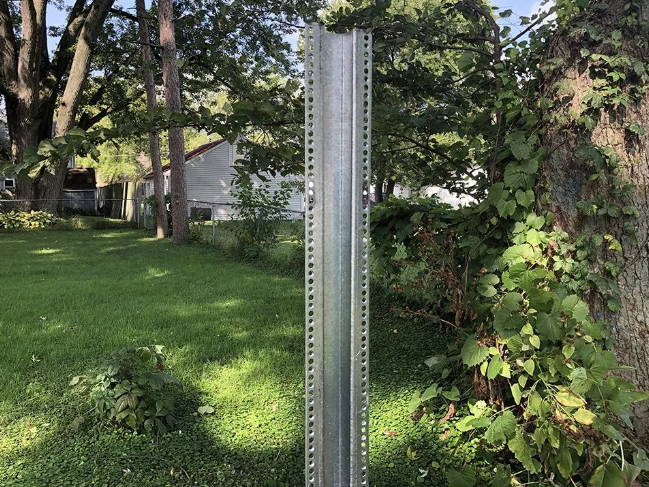 Metal signpost in a grassy yard, with trees and a house in the background.