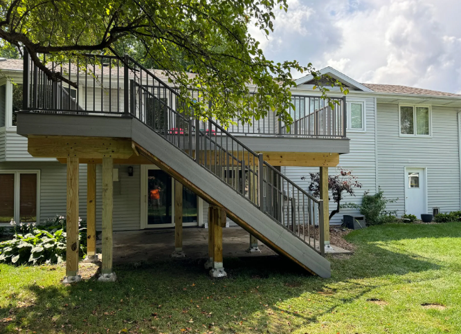 Gray composite deck with stairs attached to a two-story light-colored house.