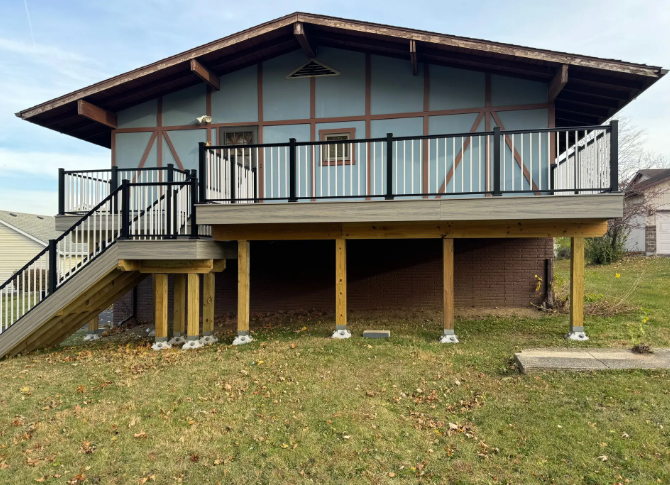 A wooden deck with black railings and stairs attached to a light blue building with brown trim.