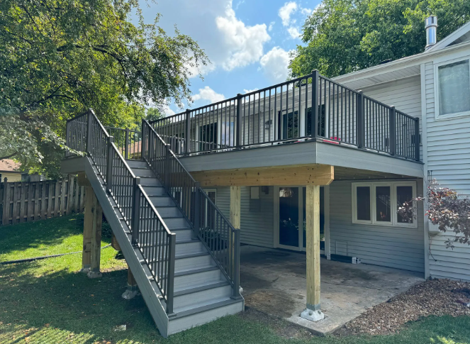 Two-story deck with stairs, gray and black railings. Exterior of a house, sunny day.