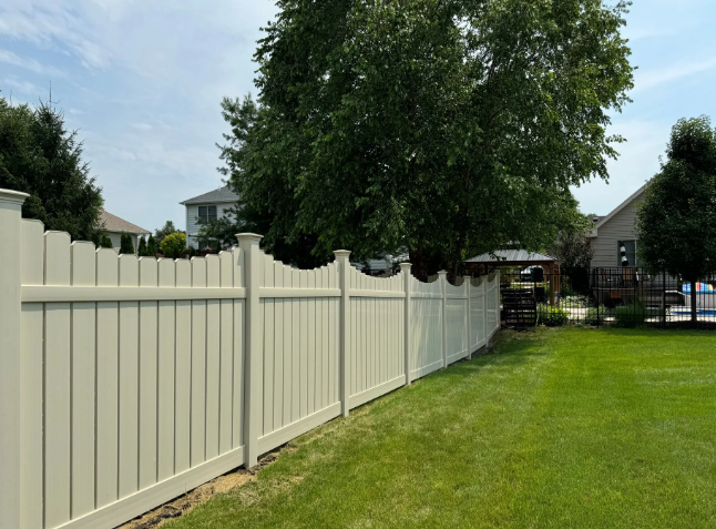 Tan vinyl fence in a grassy yard, with trees and houses in the background.