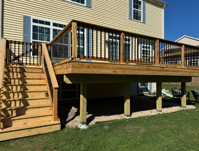 Wooden deck with stairs attached to a two-story beige house; black railing; gravel underneath.