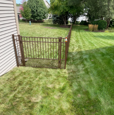 Brown metal gate in a grassy yard, next to a beige house wall.