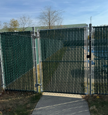 Green privacy slats on a chain-link fence with an open gate; outdoor, daylight.