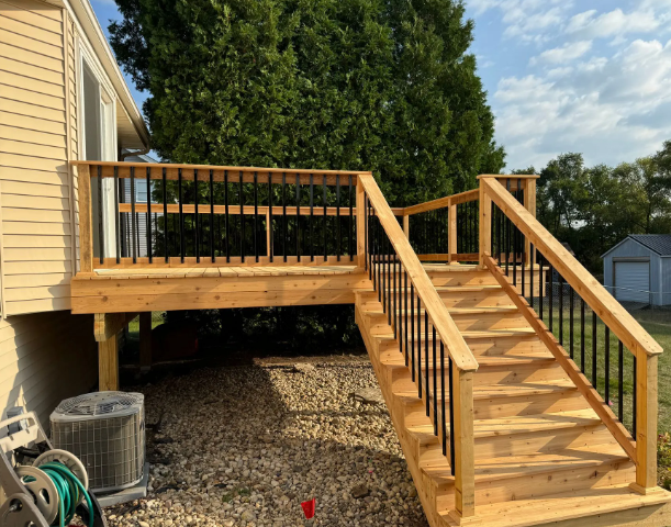 Wooden deck with stairs, black railing, attached to beige house, gravel yard.