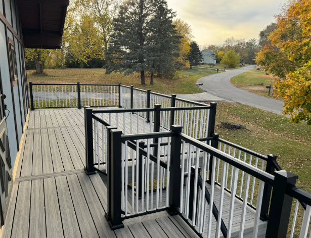 Deck with gray boards, black and white railing, overlooking a road and yard with fall foliage.