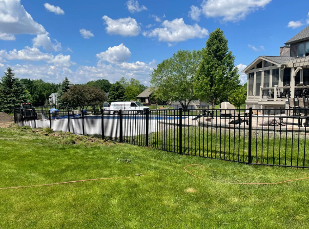 Black metal fence surrounding an above-ground pool on a grassy lawn under a sunny sky.