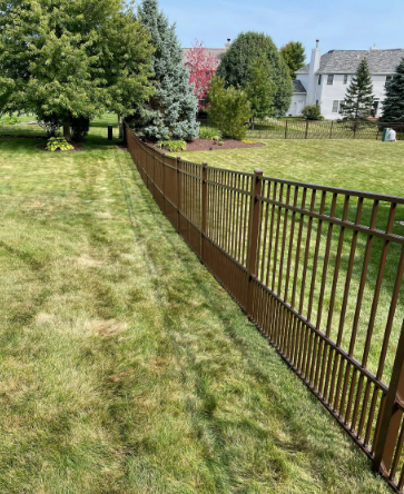 Brown metal fence along a green lawn, trees in the background, a house visible.