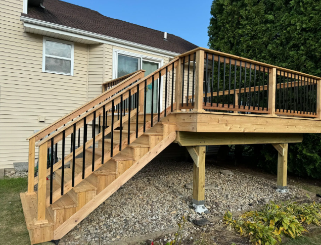 Wooden deck with black railings and stairs, built onto the side of a beige house.