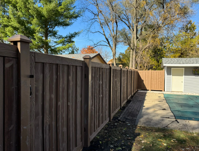 Wooden fence surrounding a backyard with a pool. Gate is visible. Trees and blue sky in the background.