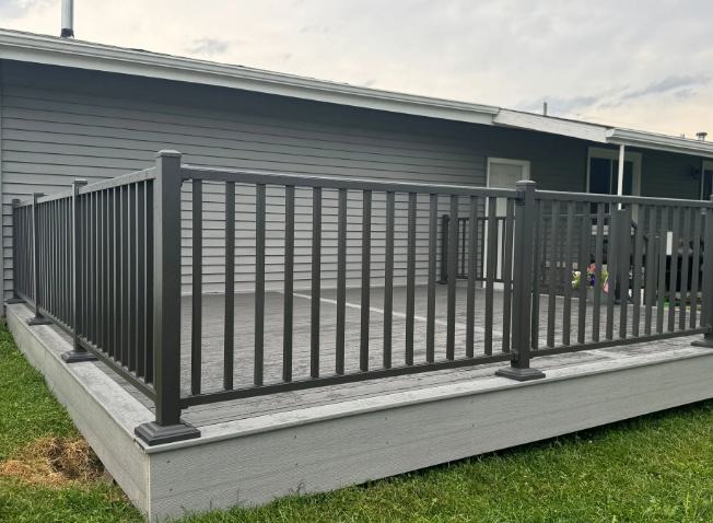 Dark gray deck with matching railing next to a gray house, set on green grass.