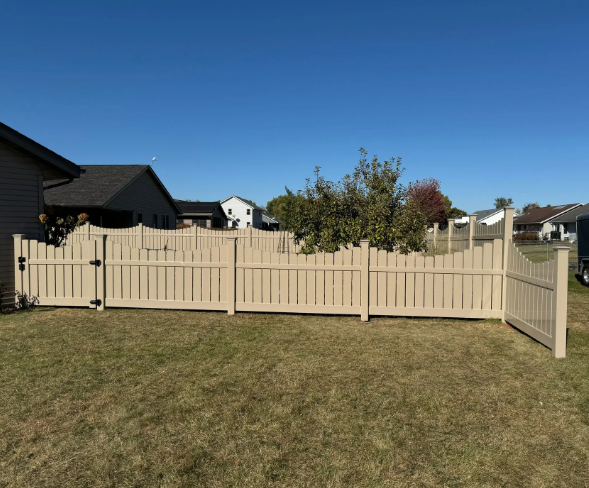 Tan vinyl fence encloses a backyard with a grassy lawn, under a blue sky.