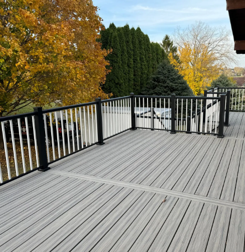 Gray composite deck with white balustrade and black posts, with fall foliage in background.