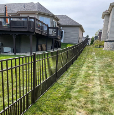 Brown metal fence along a grassy slope, separating neighboring houses with decks.
