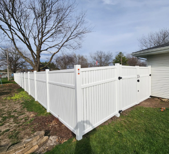 White vinyl fence encloses a backyard with green grass and a house.