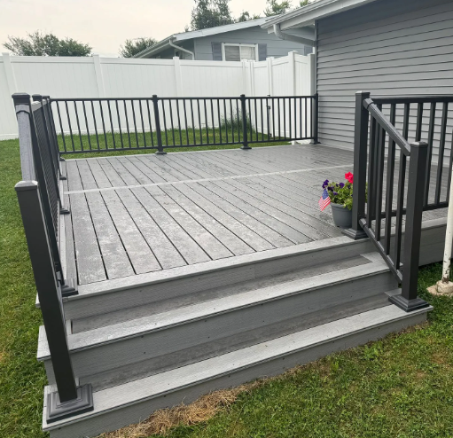 Gray composite deck with black railings and steps, overlooking a yard and white fence.