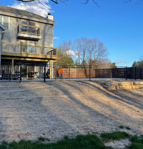 A fenced-in backyard with a deck connected to a two-story house under a blue sky.