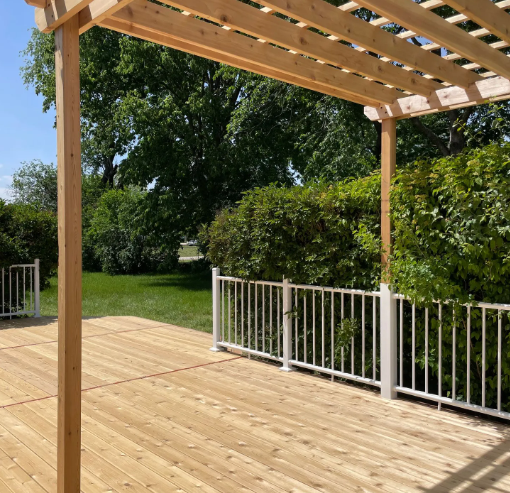 Wooden deck with pergola and white railing, overlooking a green lawn and bushes.