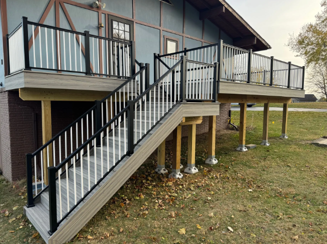 Deck with stairs and black and white railing on a house, supported by wooden posts.