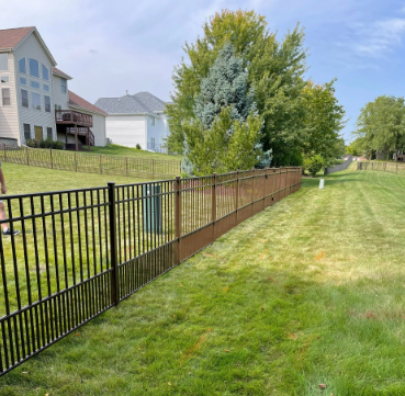Black metal fence in a grassy yard, separating properties with houses visible in the background.
