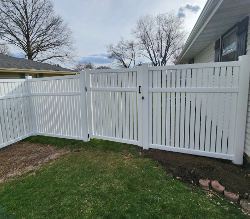 White vinyl fence with a gate in a residential backyard.