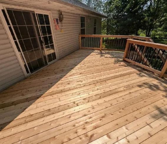 Wooden deck with railing next to a house with sliding glass door.