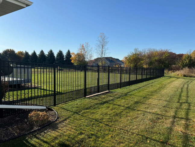 Black metal fence on a grassy lawn under a blue sky, trees in the background.
