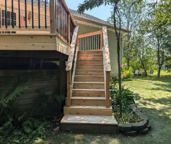 Wooden outdoor staircase leading up to a deck, set against a house and grassy yard.