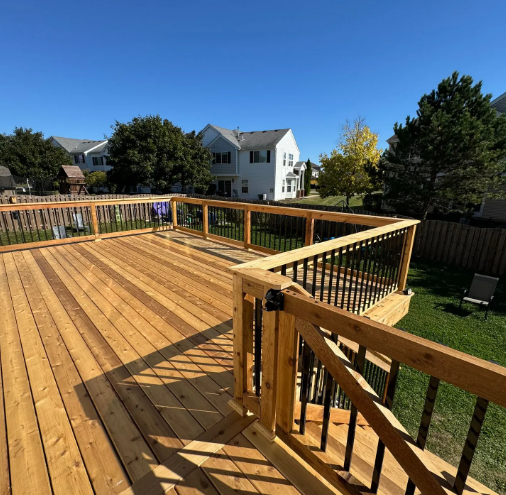 Wooden deck with black railings in a backyard on a sunny day.