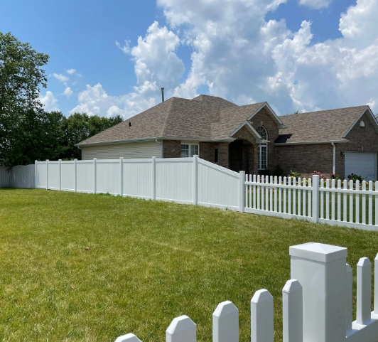 White fence around a house with a brown roof and a blue sky with fluffy clouds.