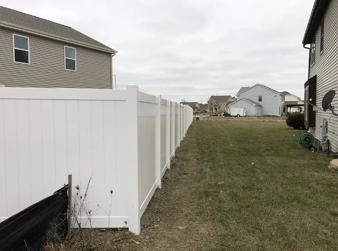 White fence borders a grassy backyard between two houses on a cloudy day.