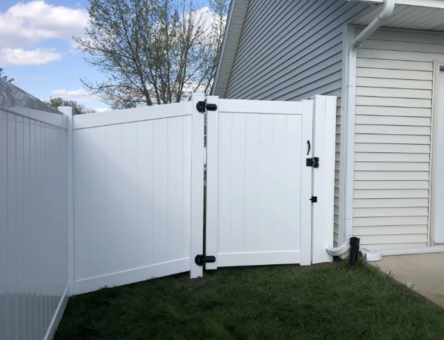 White vinyl fence with matching gate in a grassy yard, next to a building with siding.