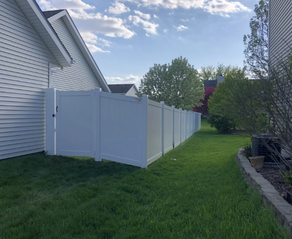 White vinyl fence beside a house with green lawn under a blue sky.
