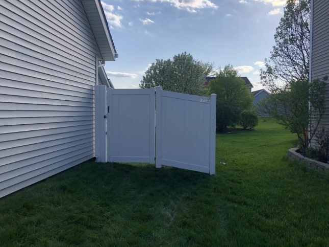 White fence against the side of a house on a grassy lawn.
